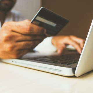 Someone holding a payment card while typing on a laptop